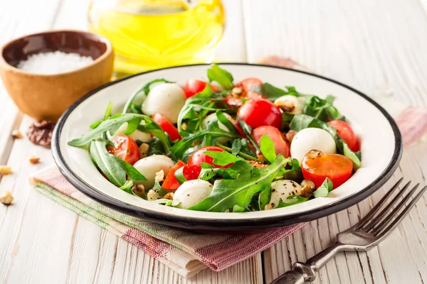 Ensalada fresca con rúcula, tomates cherry, queso mozzarella y nueces sobre fondo de madera blanca . — Foto de Stock