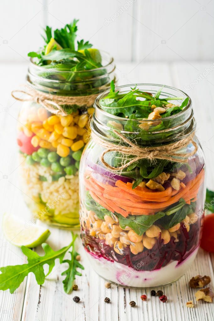 Healthy homemade salads with chickpeas, bulgur and vegetables in mason jars on white wooden background.