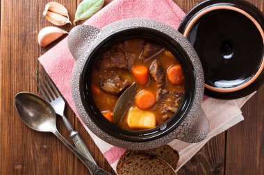 Ahşap masa üzerinde seramik tencerede sebzeli güveç et.