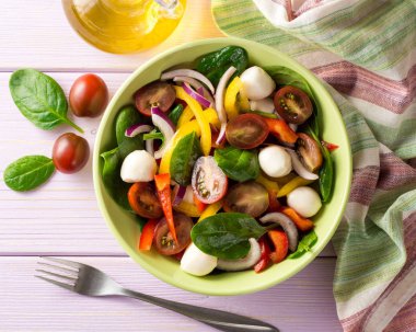 Ispanak, biber, domates, kırmızı soğan ve mozzarellalı mor ahşap zemin üzerine taze salata.