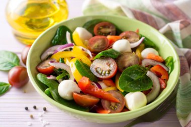 Ispanak, biber, domates, kırmızı soğan ve mozzarellalı mor ahşap zemin üzerine taze salata.