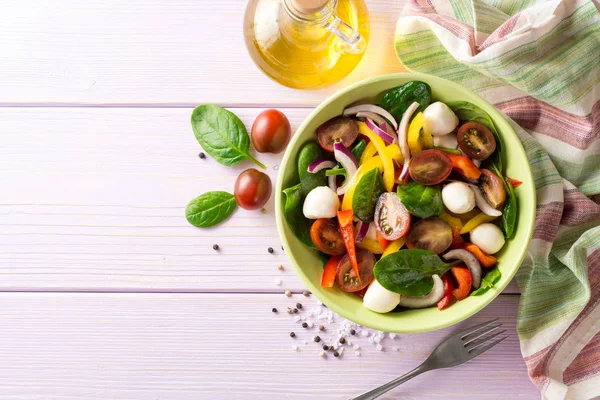 Ensalada fresca con espinacas, pimientos, tomates, cebollas rojas y mozzarella sobre fondo de madera púrpura . — Foto de Stock