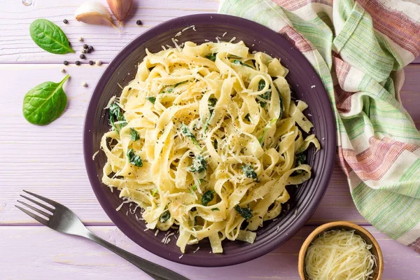 Tagliatelle-Pasta mit Spinat, Knoblauch und Parmesan auf violettem Holzgrund. — Stockfoto