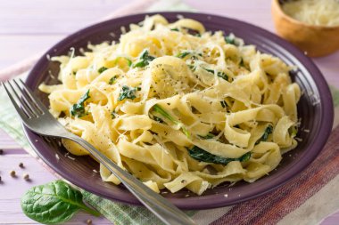Tagliatelle makarna ıspanak, sarımsak ve Parmesan peyniri mor ahşap zemin üzerine.