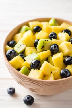 Beyaz ahşap zemin üzerinde bir yaban mersini, kivi, mango ve ananas ile taze meyve salatası.