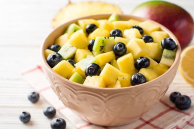 Beyaz ahşap zemin üzerinde bir yaban mersini, kivi, mango ve ananas ile taze meyve salatası.