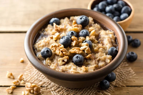 Oatmeal porridge with blueberries, walnuts and honey in ceramic bowl on wooden background.