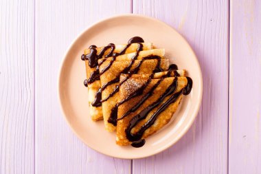 Mor ahşap zemin üzerine çikolata şurubu ile krep.