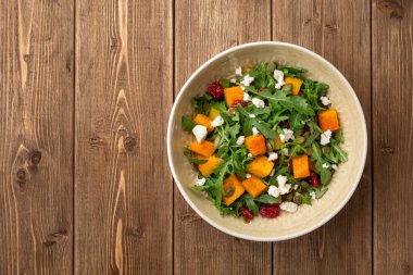 Fırında balkabağı, roka, tohumlar, kurutulmuş kızılcık ve kırsal ahşap arka planda beyaz peynir ile sonbahar salatası. Üst Manzara. Boşluğu kopyala.
