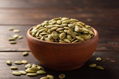 Koyu ahşap zemin üzerinde seramik kasede kabak tohumları