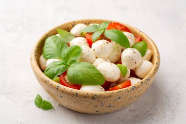 Geleneksel İtalyan caprese salatası mozzarella peyniri, kiraz domatesleri ve çimento arka planda seramik kasede fesleğen. Seçici odak.