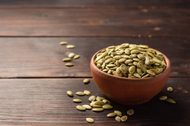 Koyu ahşap zemin üzerinde seramik kasede kabak tohumları