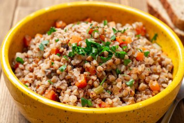 Karabuğday lapası, sebzeli ve mantarlı. Kırsal ahşap masadaki seramik kasede. Seçici odak.