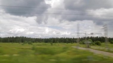 Tren araba penceresinden görünümü. Yaz günü, bulutlar, yeşil ağaçlar, enerji hatları, demiryolu geçiş