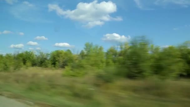 Летний или осенний пейзаж за окном автобуса или автомобиля. Солнечный день, зеленая растительность, облака на голубом небе — стоковое видео