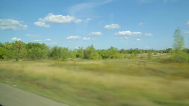 Летний или осенний пейзаж за окном автобуса или автомобиля. Солнечный день, зеленая растительность, облака на голубом небе — стоковое видео