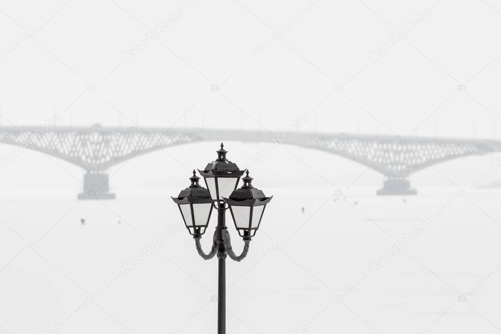 Street lamp on the background of the bridge across the Volga. Winter day, Saratov, Russia