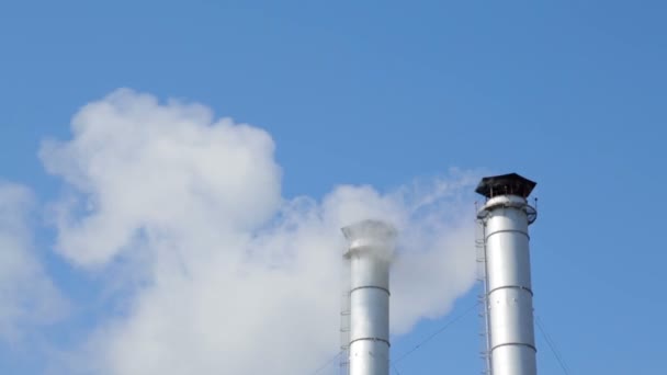 De rook van de schoorstenen van een verwarmingsinstallatie in de achtergrond van de blauwe hemel. — Stockvideo