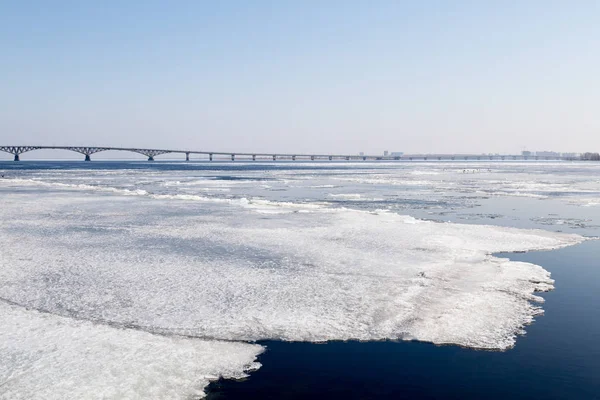 O gelo da primavera deriva no rio Volga. Ponte rodoviária na cidade de Saratov. A Rússia. Um dia ensolarado em Março. Céu azul — Fotografia de Stock