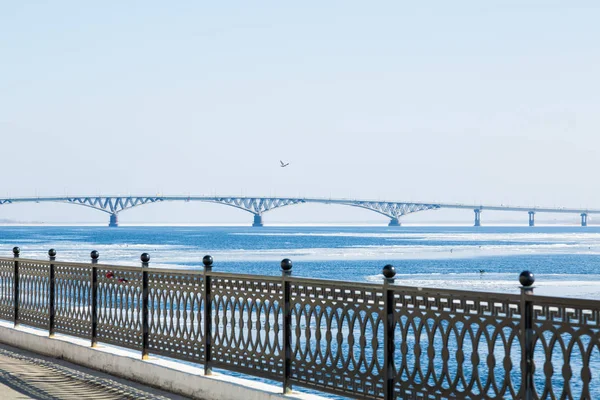 O gelo da primavera deriva no rio Volga. Ponte rodoviária na cidade de Saratov. A Rússia. Um dia ensolarado em Março. Céu azul. Cerca de ferro fundido na orla — Fotografia de Stock