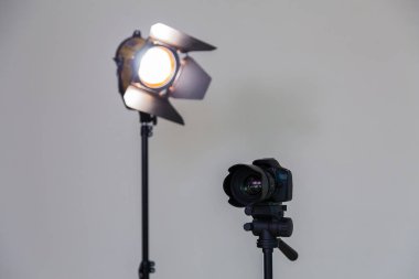 Digital SLR camera and a spotlight with a Fresnel lens on a gray background. Shooting in the interior. Equipment for the production of films clipart