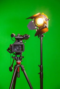 A video camera and a spotlight with a Fresnel lens on a green background. Filming in the interior. The chroma key clipart
