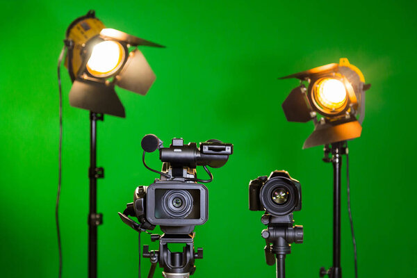 Two spotlights with Fresnel lenses, camcorder and SLR camera on a green background. Shooting in the interior with artificial light. The chroma key