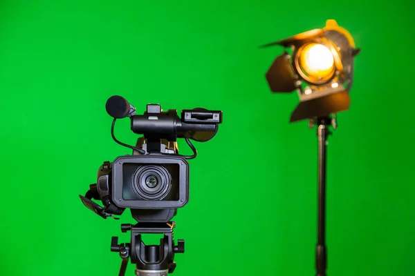 En videokamera och en spotlight med en fresnellins på en grön bakgrund. Filmning i inredningen. Färgtransparens — Stockfoto
