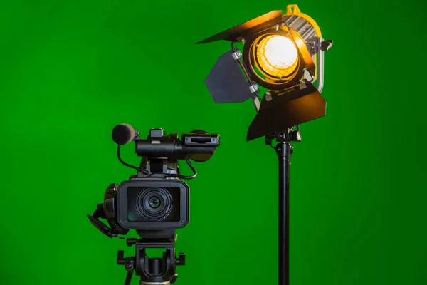 Una videocamera e un faretto con una lente Fresnel su sfondo verde. Le riprese all'interno. La chiave cromatica — Foto Stock