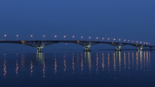 Повний місяць піднімається над мостом. Уповільнена. Автомобільного мосту між містами Саратов і Енгельс, Росія. Волги. Увечері вогні автомобілів і вуличних ліхтарів. 4 Кбайт, Ultra Hd — стокове відео