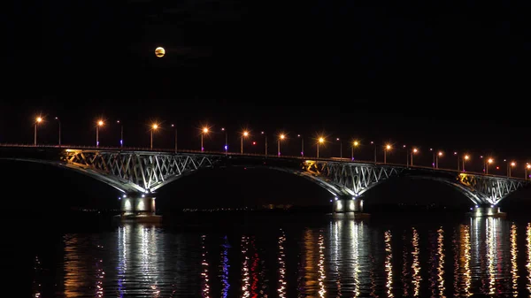 Úplněk se tyčí nad mostem. Silniční most mezi městy Saratov a Engels, Rusko. Řeka Volha. Večer světel aut a pouliční osvětlení — Stock fotografie