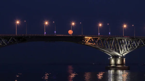 満月は、橋を上昇.サラトフの都市とエンゲルス、ロシアの道路橋。ヴォルガ川。車と街路灯の夜灯 — ストック写真