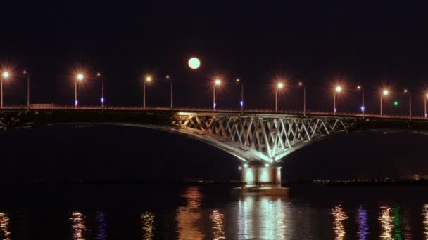 Повний місяць піднімається над мостом. Уповільнена. Автомобільного мосту між містами Саратов і Енгельс, Росія. Волги. Увечері вогні автомобілів і вуличних ліхтарів. 4 Кбайт, Ultra Hd — стокове відео
