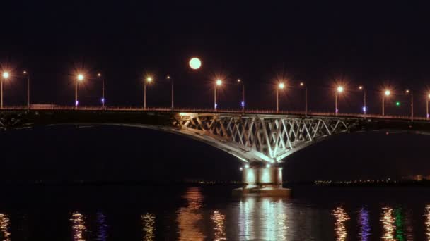 A lua cheia sobe sobre a ponte. Desfasamento de tempo. Ponte rodoviária entre as cidades de Saratov e Engels, Rússia. O rio Volga. As luzes noturnas de carros e luzes de rua. 4K, Ultra HD — Vídeo de Stock