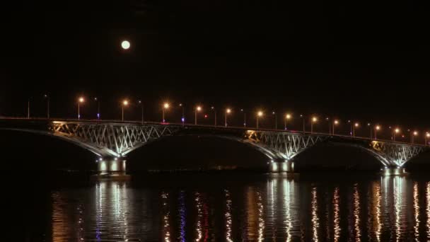 La luna piena sorge sul ponte. Un time-lapse. Ponte stradale tra le città di Saratov ed Engels, Russia. Il fiume Volga. Le luci serali di auto e lampioni. 4K, Ultra HD — Video Stock