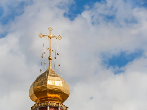 The Golden dome of an Orthodox temple on background of blue sky and clouds. Golden cross on the dome of the temple