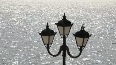 Bir nehir veya deniz önünde sokak lambası. Güneş su parlak. 4k, Uhd, Ultra Hd