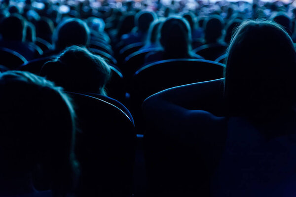 People, children, adults, parents in the theater watching the performance. People in the auditorium looking at the stage. Shooting from the back