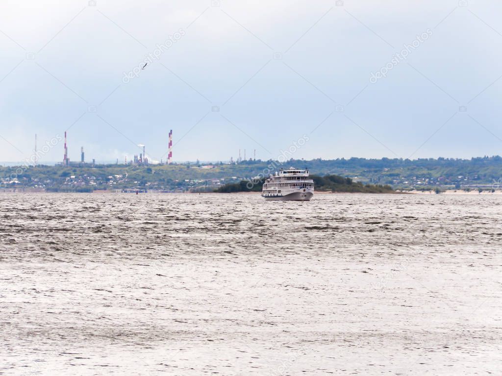 Passenger river ship on the horizon. Russia, Saratov, the Volga river. Smokestacks in the background.