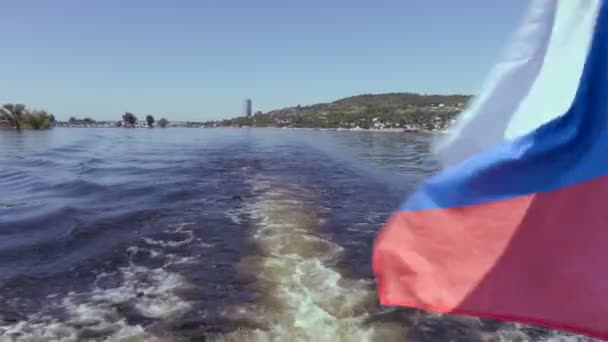 Filming from the stern of the ship. Summer river landscape. The Volga river in Saratov, Russia. Russian flag, the tricolor. Road bridge between the cities of Saratov and Engels — Stock Video