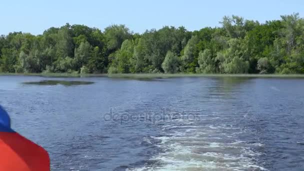 Прапор Росії на кормі судна. І слідів на воді хвилі. Річки або озера на літній день. Синє небо. Зеленої рослинності на березі. Звук мотора човни. Кадри кліпу 4 Кбайт, Ultra Hd — стокове відео