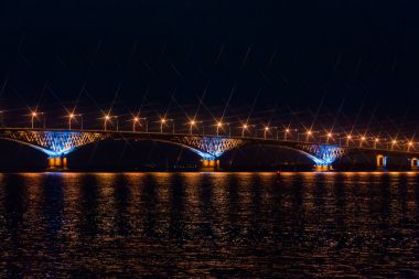 Volga Nehri Saratov şehirler ve Engels, Rusya arasındaki yolu köprüsü. Gece veya akşam manzara. Altın sokak ışıkları. Su yansıması