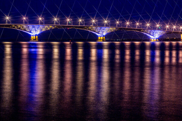 Дорожный мост через Волгу между городами Саратов и Энгельс, Россия. Ночной или вечерний пейзаж. Золотые фонари. Отражение в воде Стоковое Фото