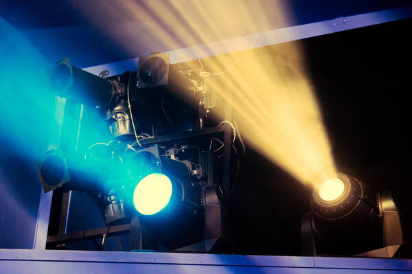 Lighting equipment on the stage of the theatre during the performance. The light rays from the spotlight through the smoke. Blue and yellow rays of light