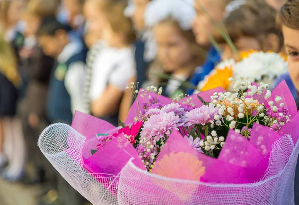 小学生の手に花の花束。学校の庭 9 月最初の式。ロシアの学校で学年の初め。背景をぼかし。前景に焦点を当てます。背景をぼかした写真 — ストック写真