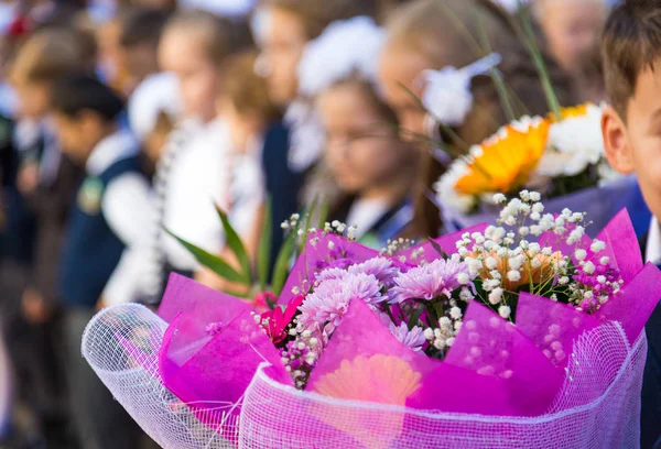 A bouquet of flowers in the hands of elementary school students. A ceremony in the school yard on the first of September. Beginning of the school year in a Russian school. Blurred background. Focus on the foreground. Blurred background