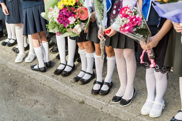 小学的女生手里拿着一束花。她脚上的鞋子和白色的裤袜、袜子和长袜。学年开始时在学校操场举行的活动。俄罗斯 — 图库照片