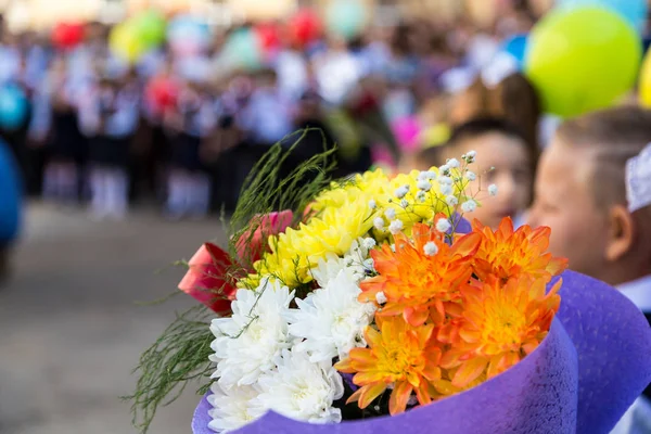 A bouquet of flowers in the hands of elementary school students. A ceremony in the school yard on the first of September. Beginning of the school year in a Russian school. Blurred background. Focus on the foreground. Blurred background