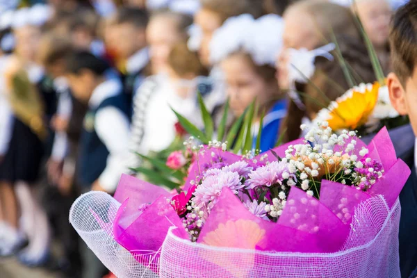 小学生の手に花の花束。学校の庭 9 月最初の式。ロシアの学校で学年の初め。背景をぼかし。前景に焦点を当てます。背景をぼかした写真 — ストック写真