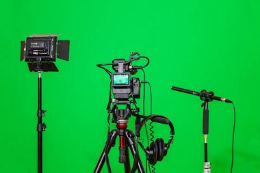 Kameranın tripod, led projektör, kulaklık ve bir yönlü mikrofon yeşil bir arka plan üzerinde. Chroma anahtar. Yeşil ekran